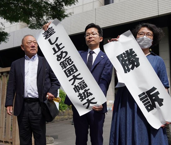 原告や支援者らに向け弁護団が「勝訴」を掲げる（6月28日・東京）