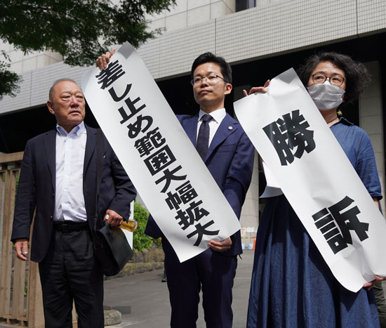 原告や支援者らに向け弁護団が「勝訴」を掲げる（6月28日・東京）